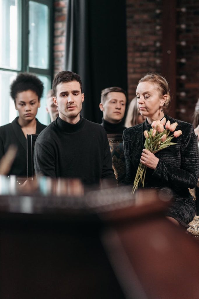 A solemn group of people attending a funeral, expressing grief and holding flowers.