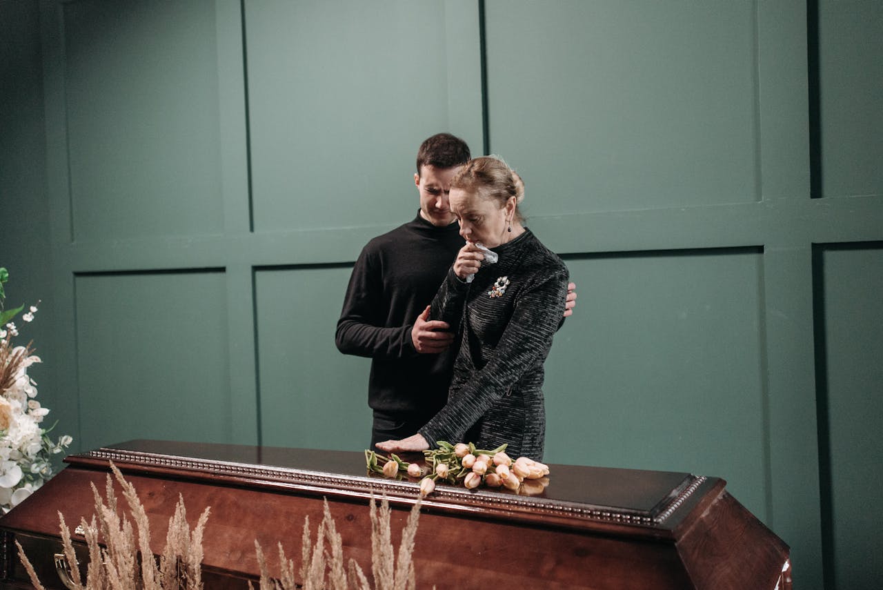 Grieving family members stand solemnly beside a coffin during a funeral.